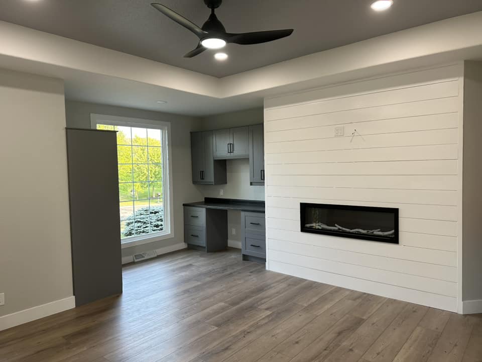 Finished sitting room with shiplap accent wall, linear electric fireplace insert, built-in gray cabinetry, and tray ceiling